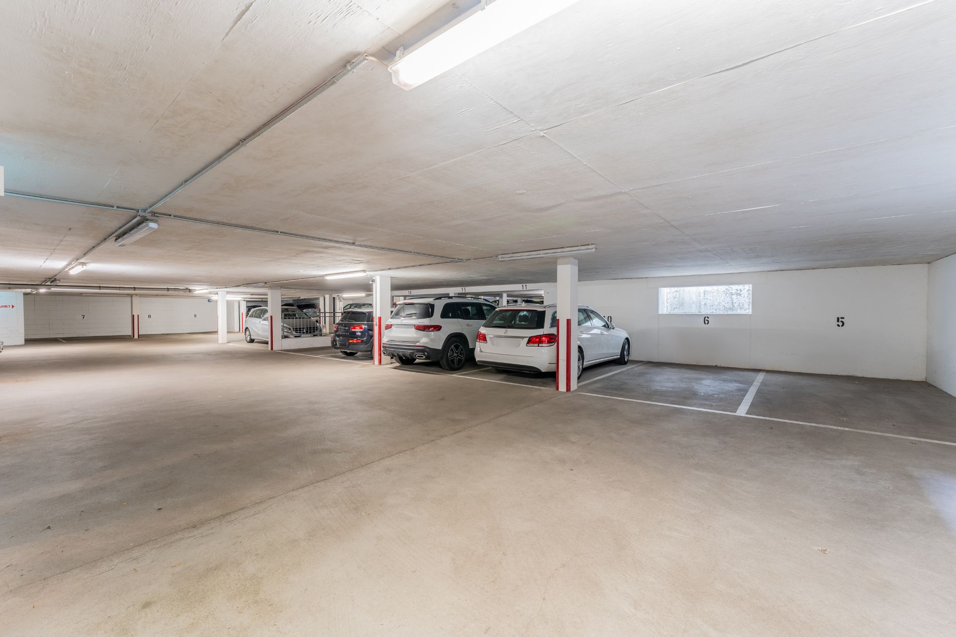 Helle Tiefgarage mit mehreren parkenden Autos und nummerierten Stellplätzen.