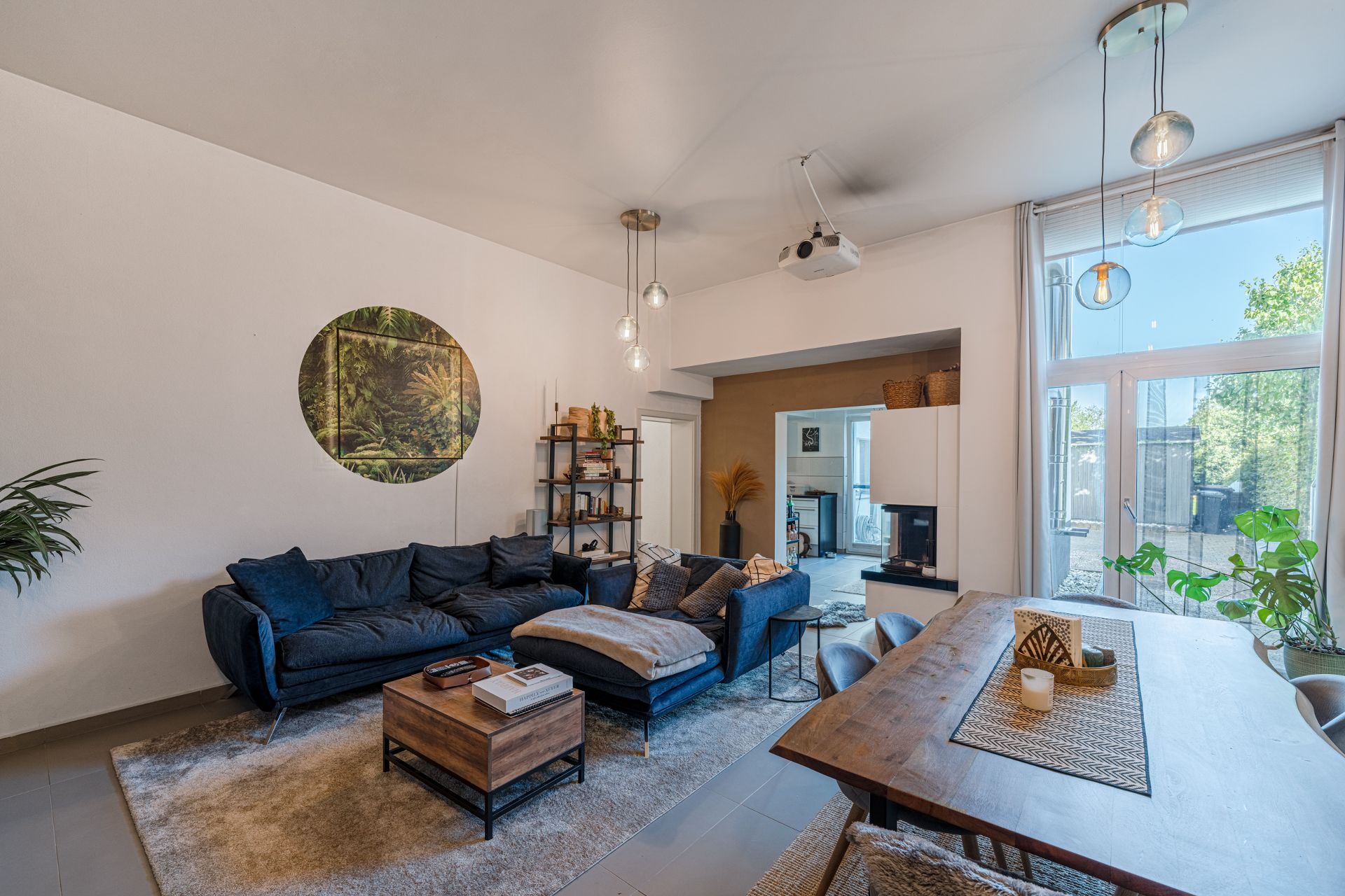 Helles Wohnzimmer mit dunkelblauem Sofa, Holztisch, Regalen und großen Fenstern.