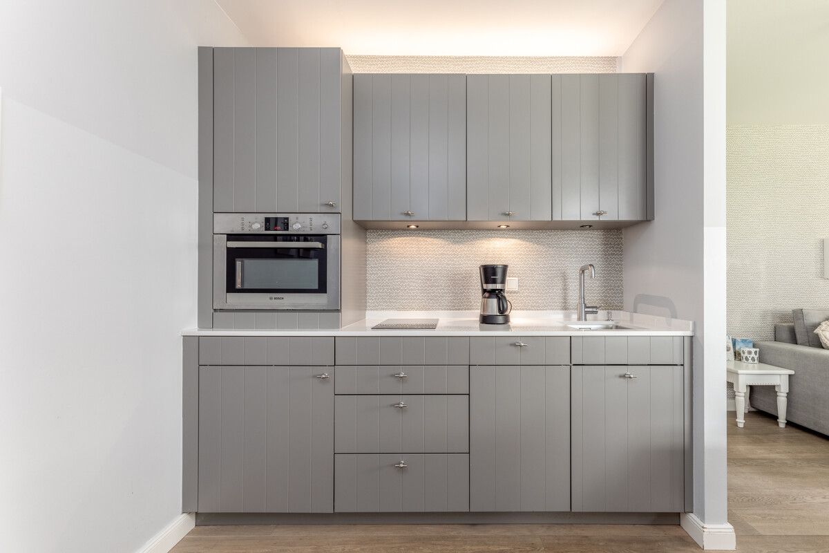 Moderne Einbauküche mit grauen Schränken, Backofen, Herd, Kaffeemaschine und Spüle.