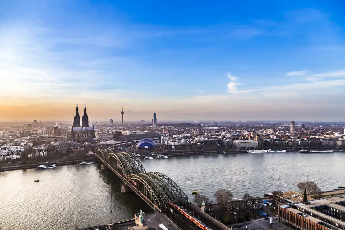 Stadtansicht mit Fluss, großer Kathedrale und Bogenbrücke bei Sonnenuntergang.