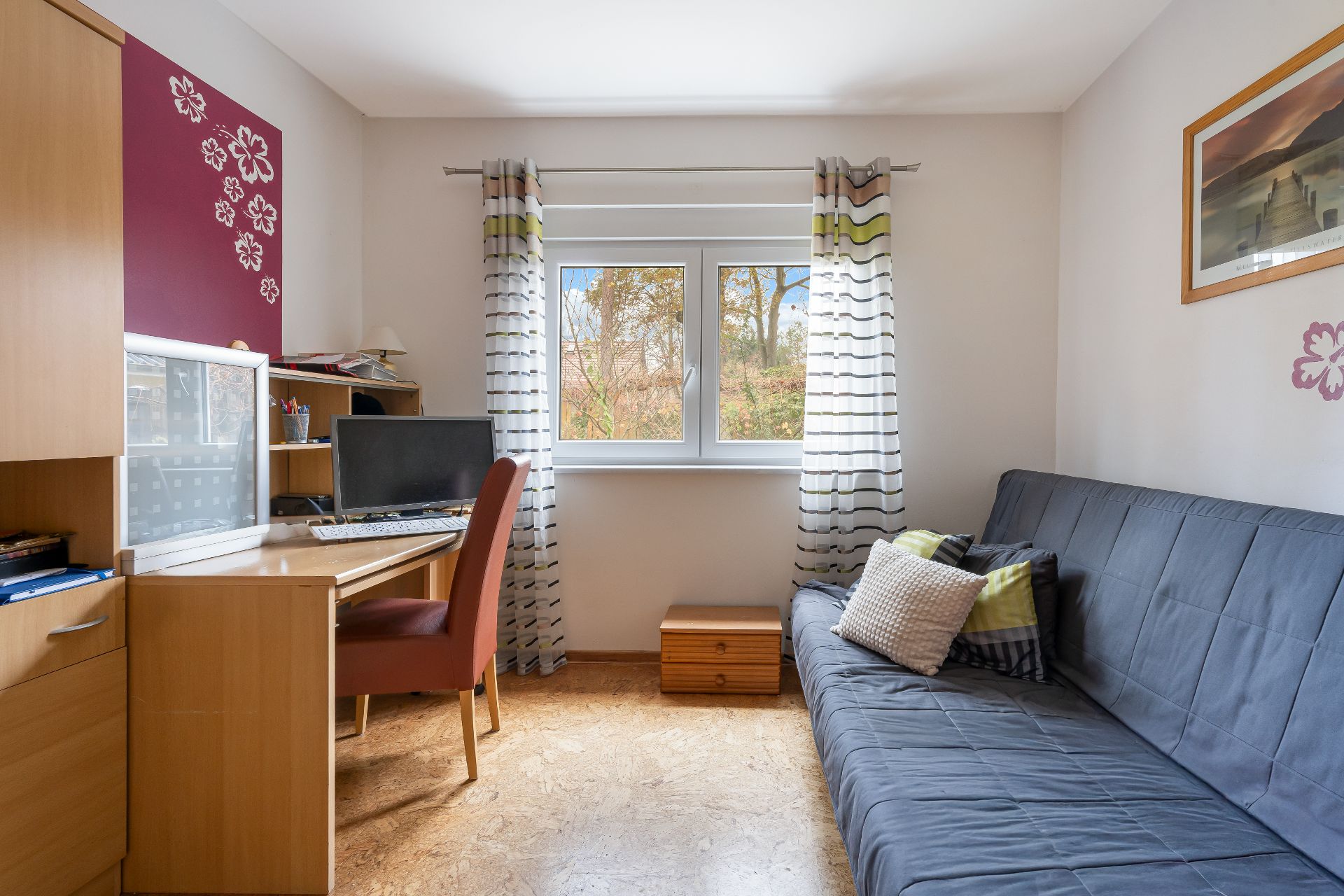 Kleines Arbeitszimmer mit Schreibtisch, Computer, Sofa und Fenster mit Vorhängen.