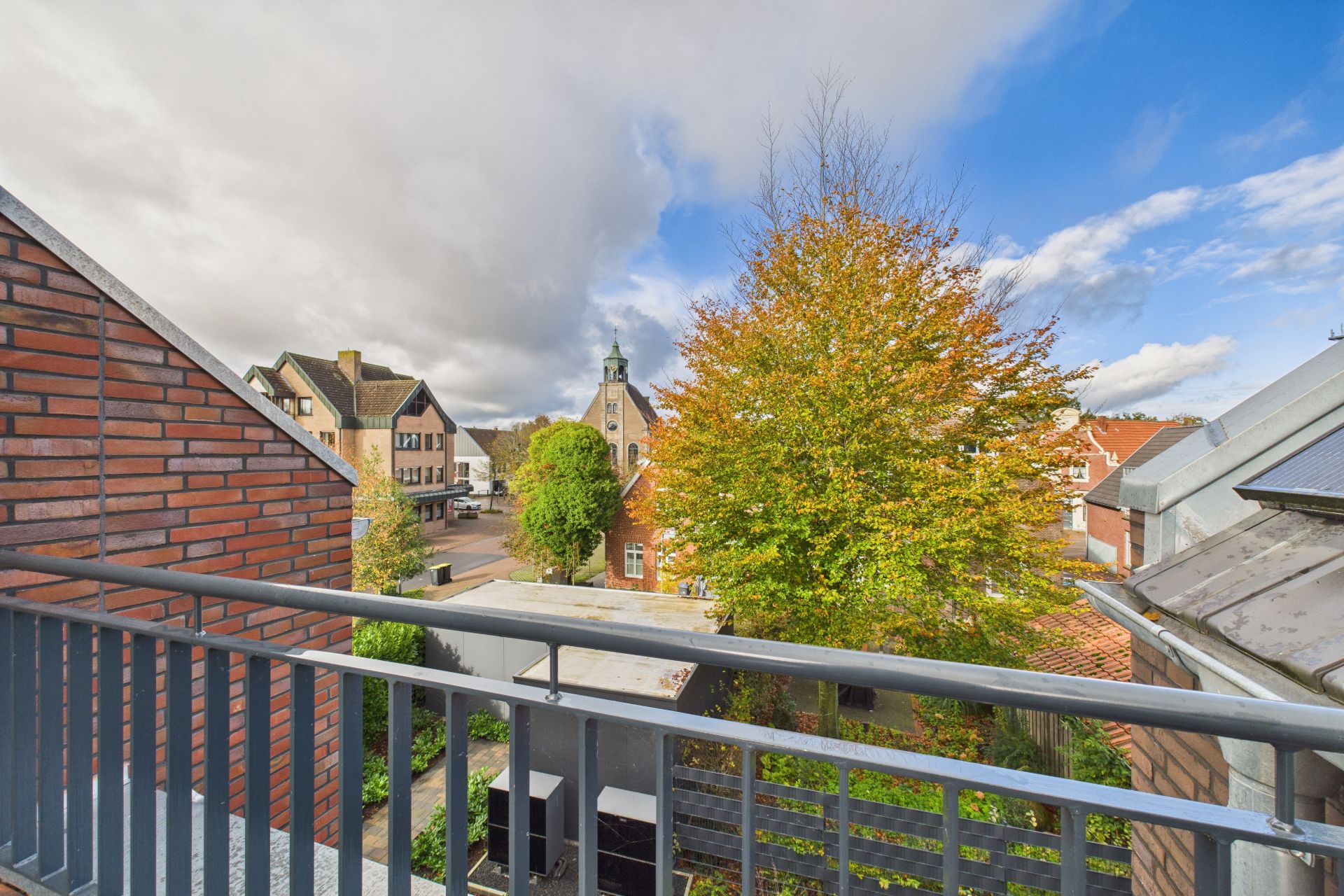Blick von einem Balkon auf Bäume, Dächer und eine ruhige Wohnstraße.