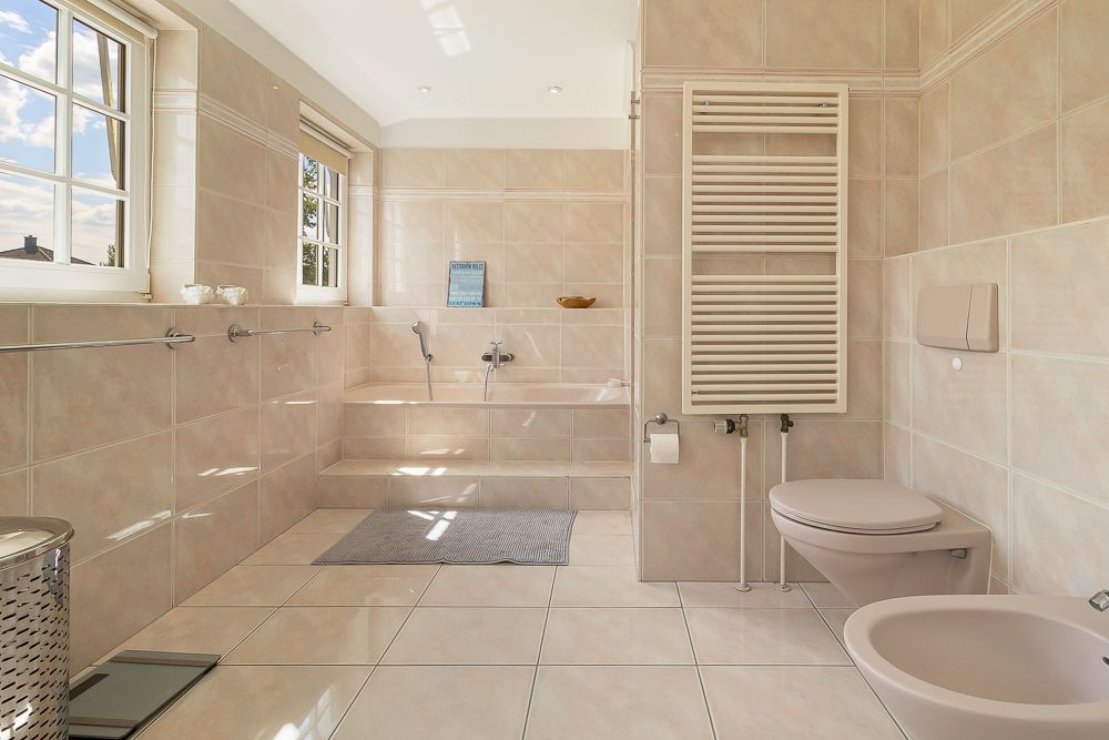 Helles Badezimmer mit Badewanne, großem Fenster, Toilette und Handtuchheizkörper.