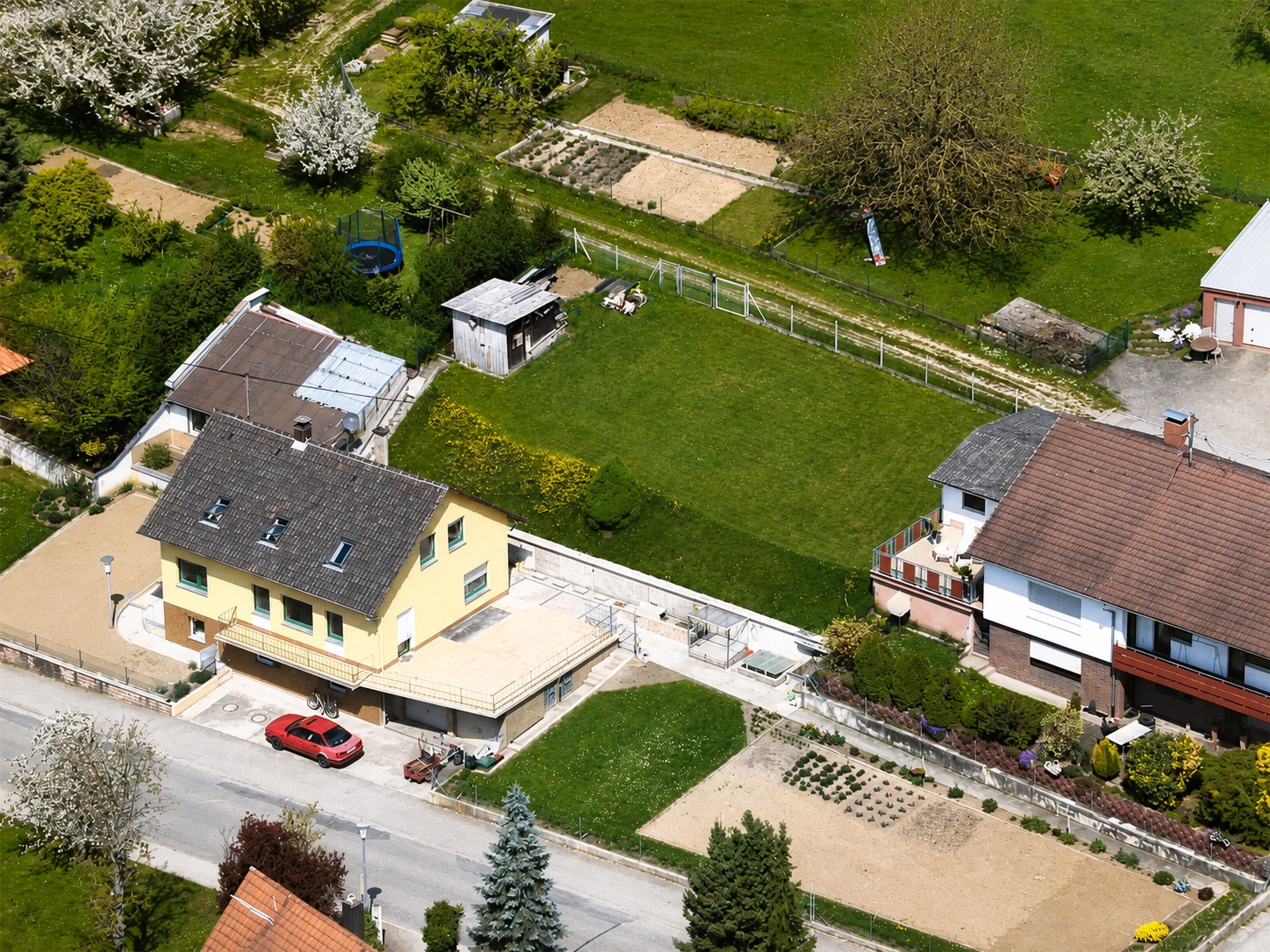 Luftaufnahme von zwei Einfamilienhäusern mit Gärten und einem roten Auto auf einer Einfahrt.