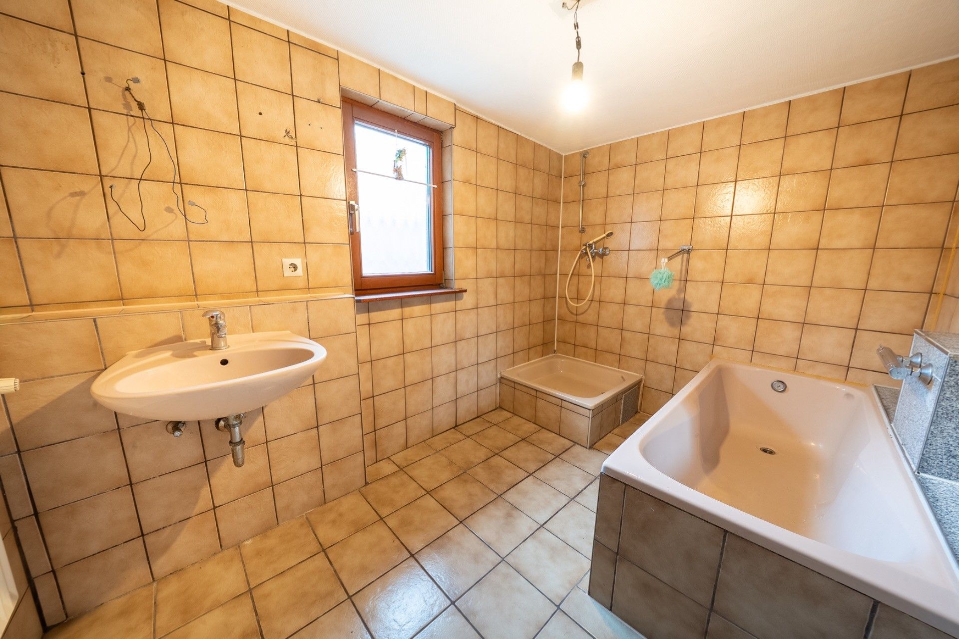 Badezimmer mit beiger Fliesen, Waschbecken, Fenster, Dusche und Badewanne.