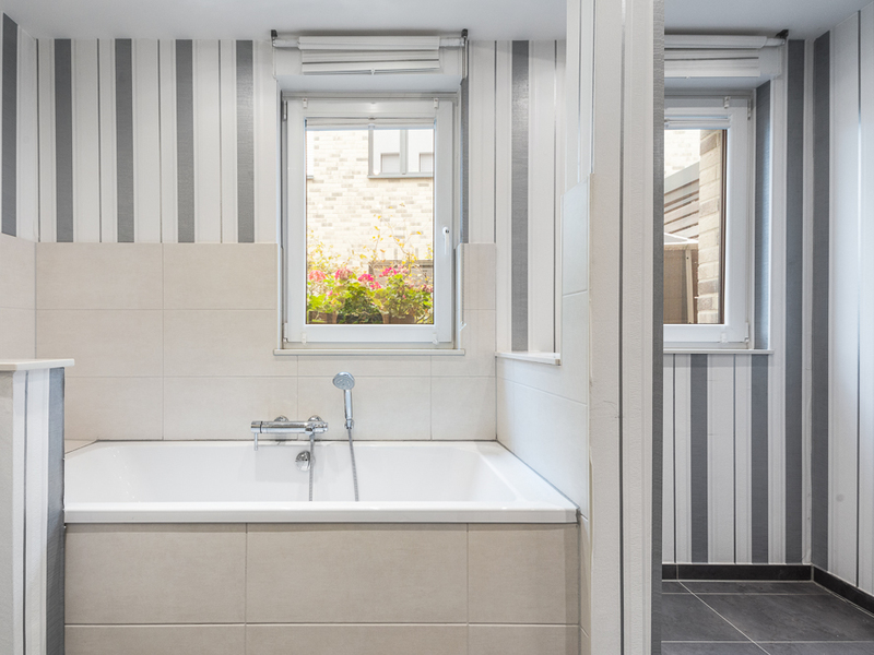 Modernes Bad mit Badewanne, gestreiften Wänden und zwei Fenstern.