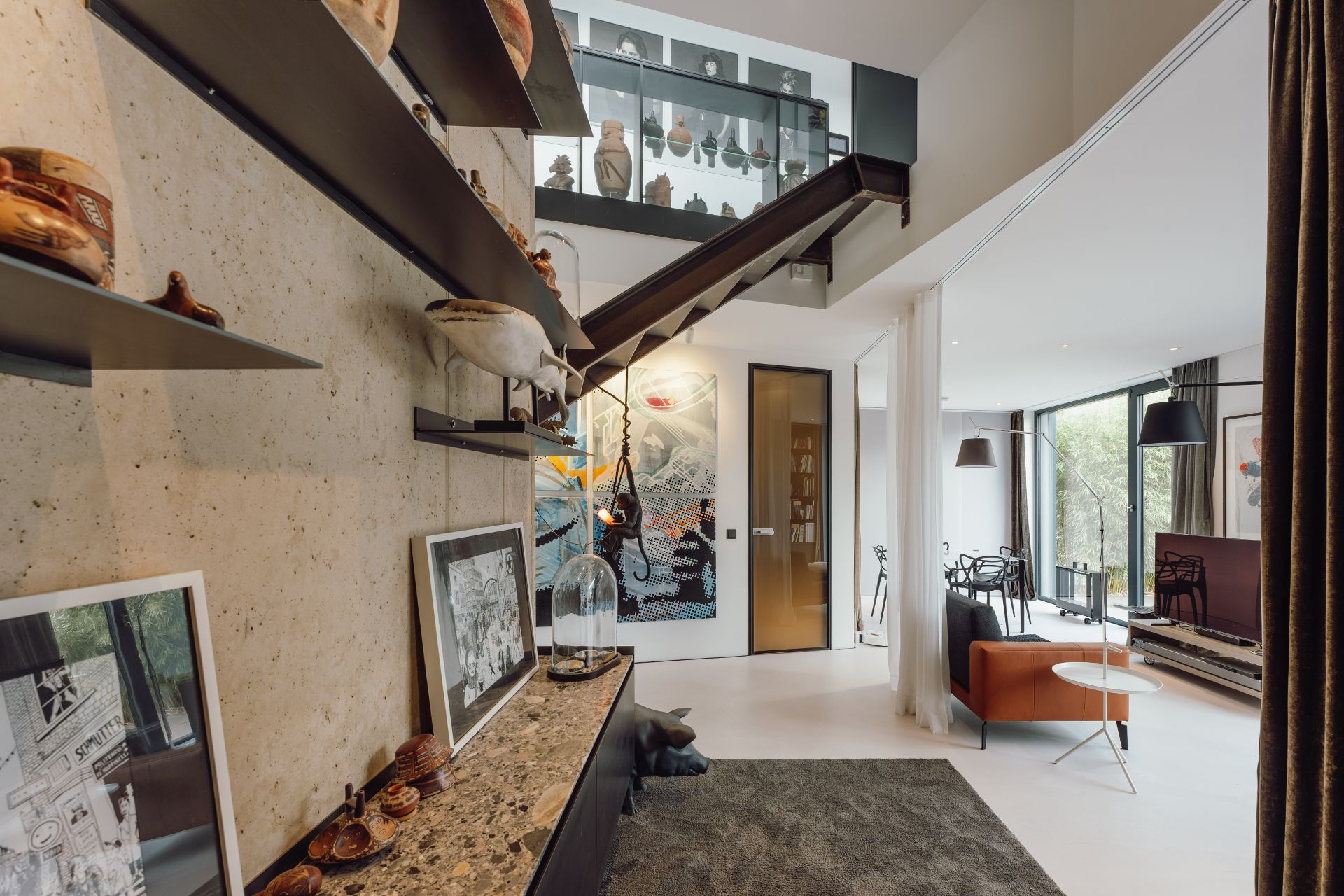 Wohnzimmer mit moderner Einrichtung, Kunstwerken, Regalen und großen Fenstern.