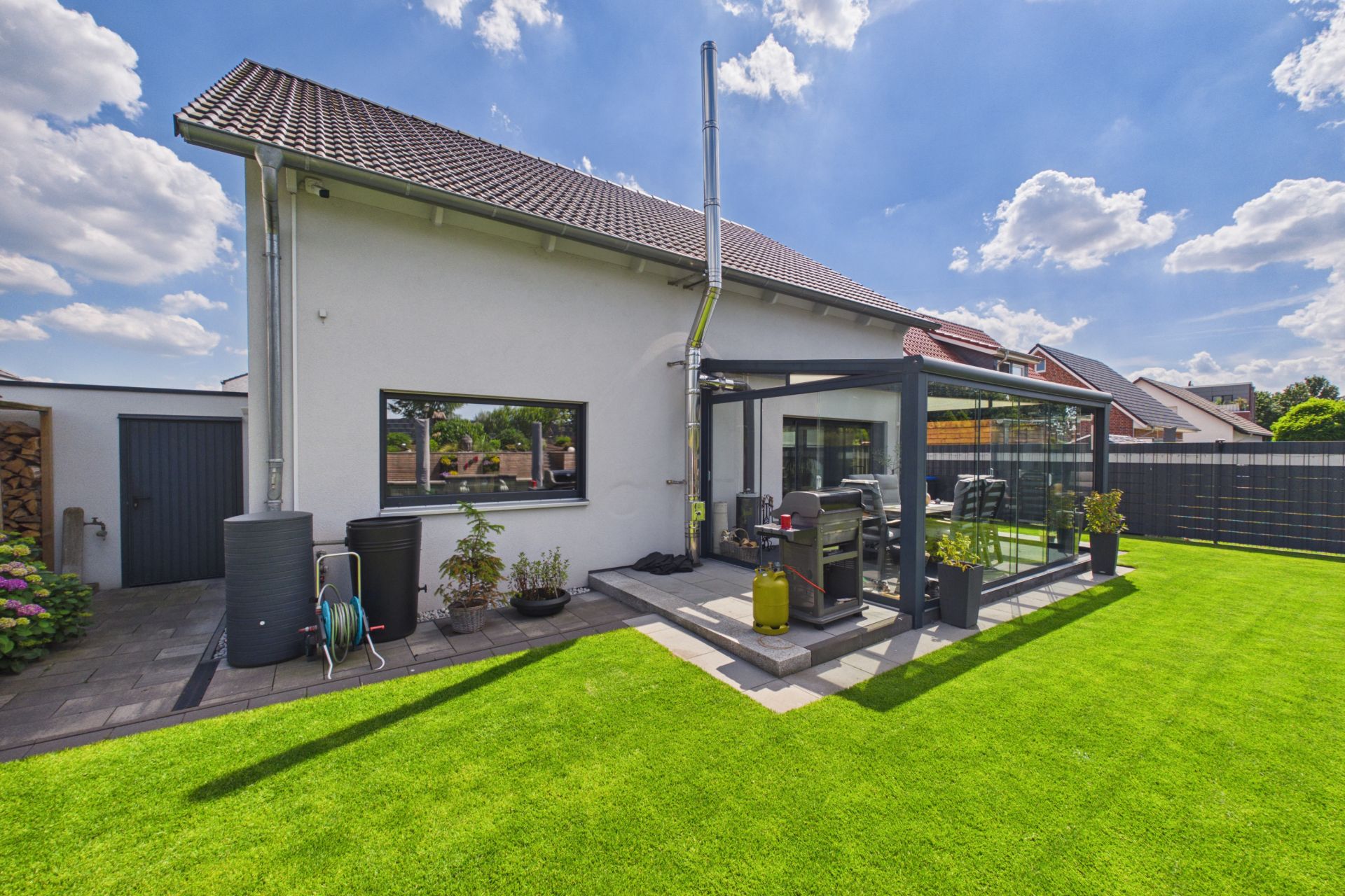 Modernes Einfamilienhaus mit Wintergarten und gepflegtem Rasen im Garten bei sonnigem Wetter.