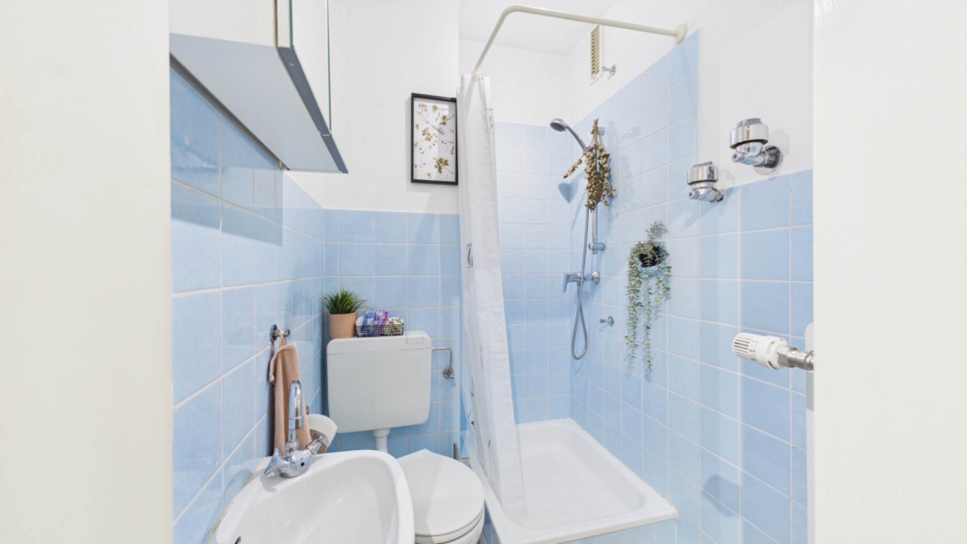 Kleines Badezimmer mit blauen Fliesen, Dusche, Toilette und Waschbecken.