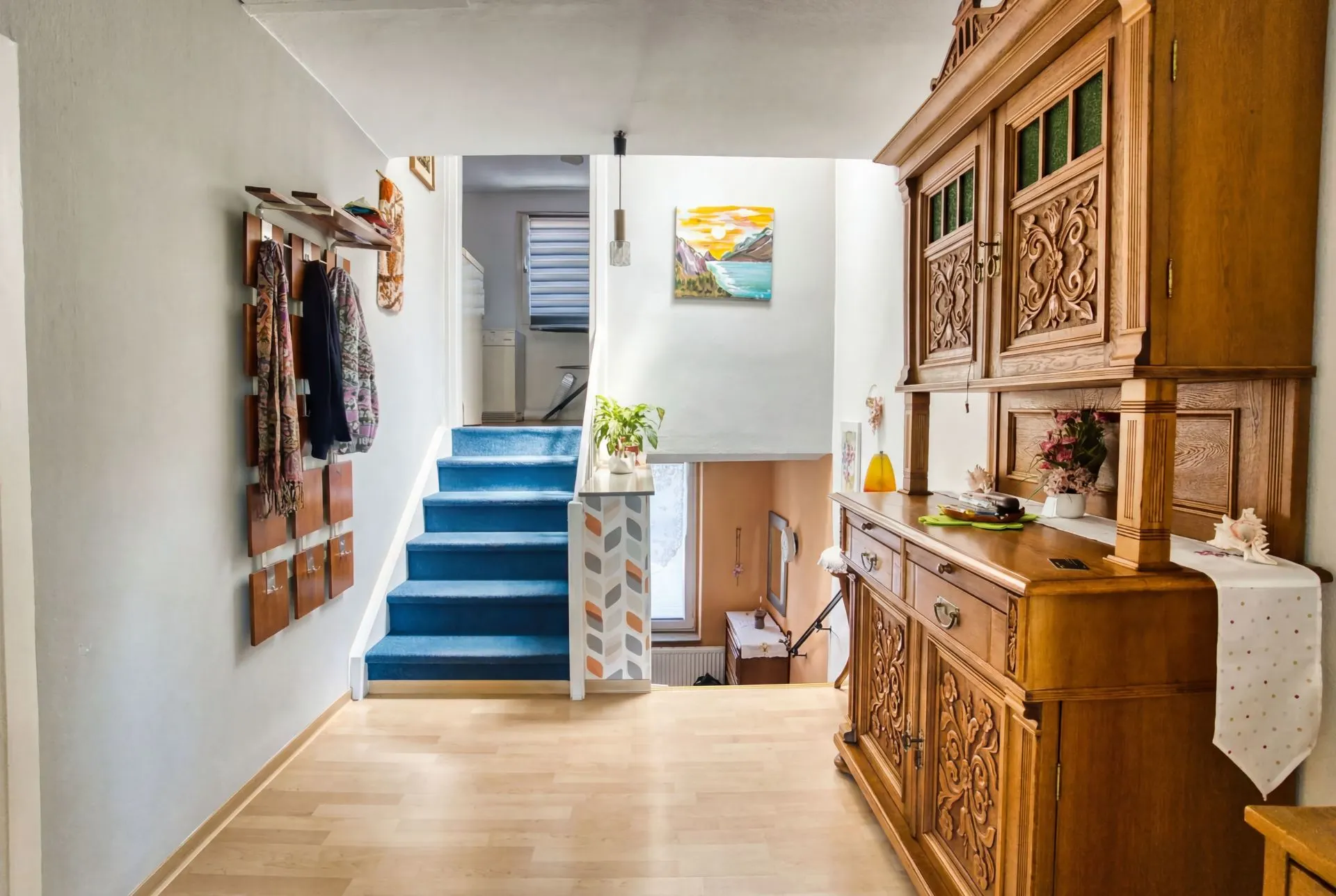 Flur mit Holzschrank, Garderobe und blauer Treppe zu oberen Räumen.