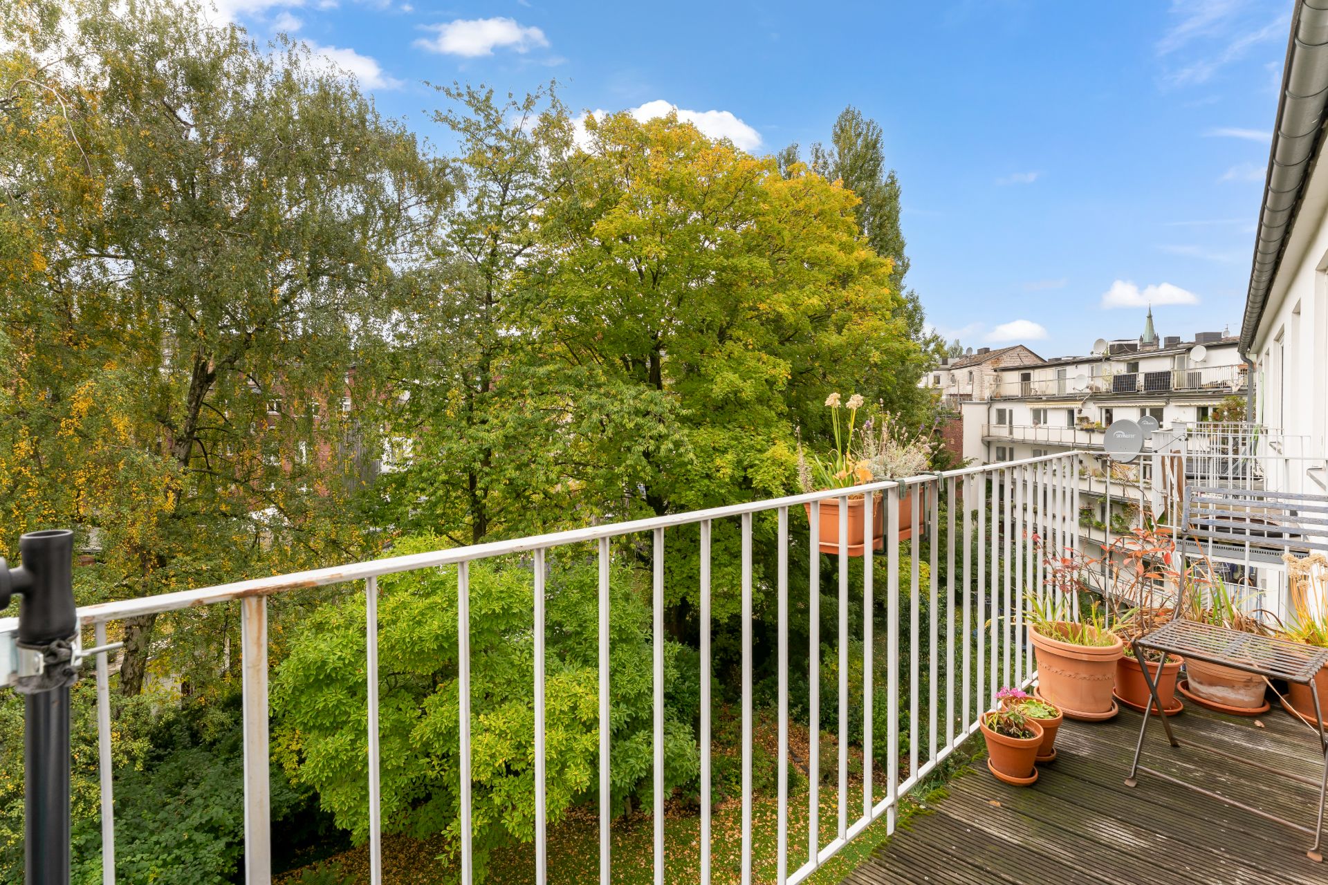 Balkon mit Blumentöpfen und Blick auf grüne Bäume und Nachbarhäuser.