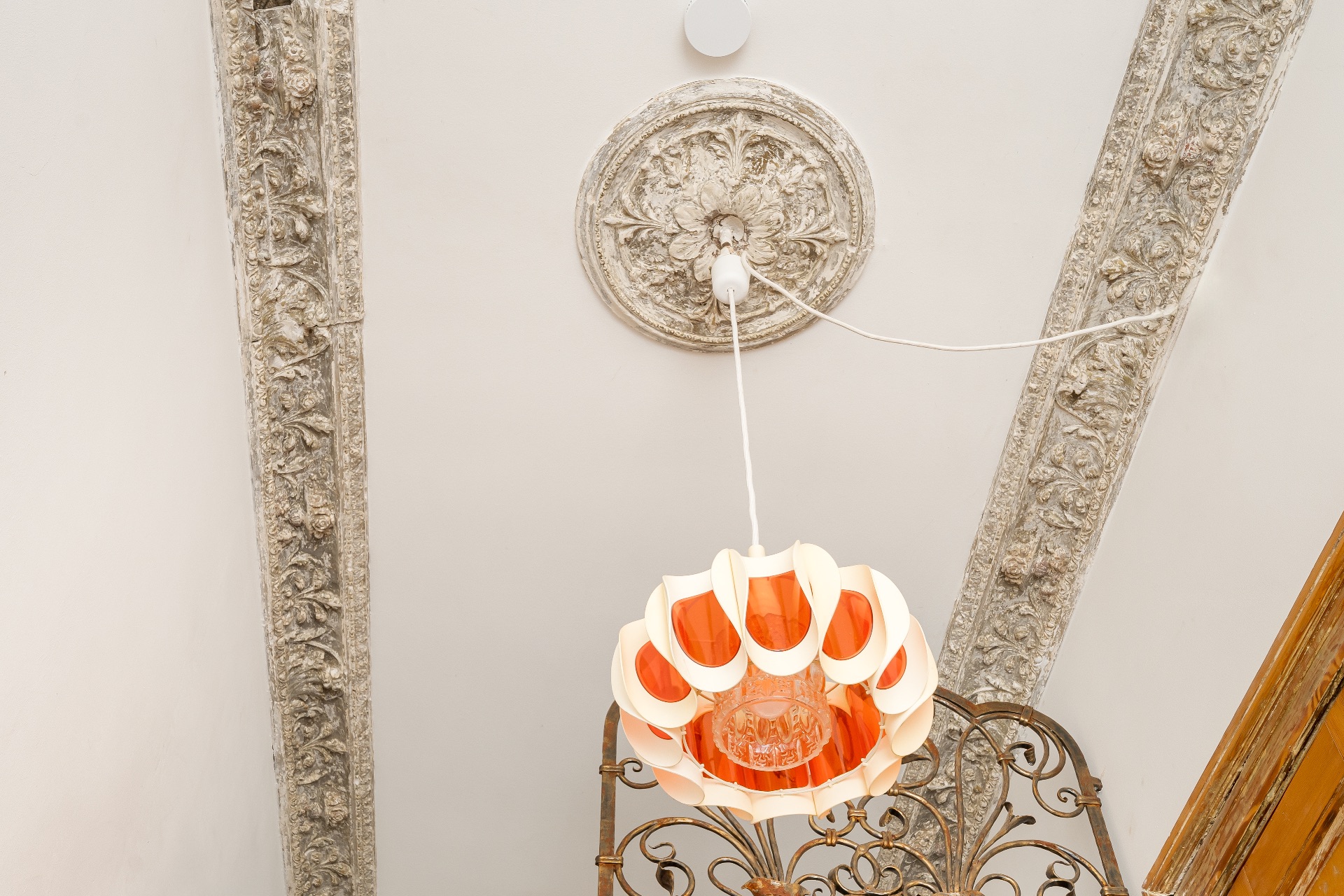 Decke mit Stuckverzierungen und einer modernen, orange-weißen Hängelampe.