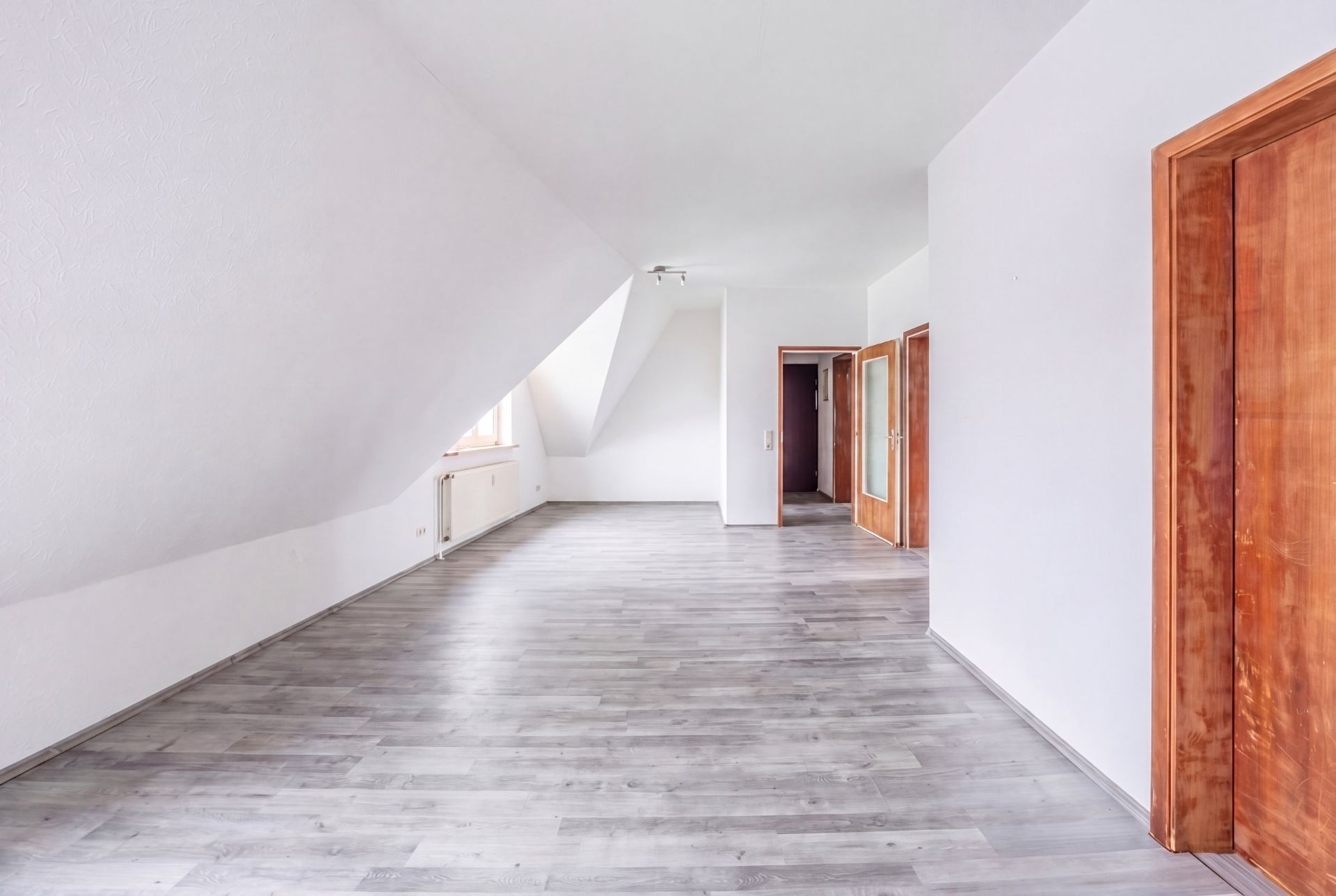 Leeres Zimmer mit Dachschräge, grauem Boden und mehreren Holztüren.
