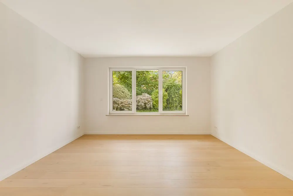 Leerer Raum mit hellem Holzboden und großem Fenster mit Blick auf Garten.