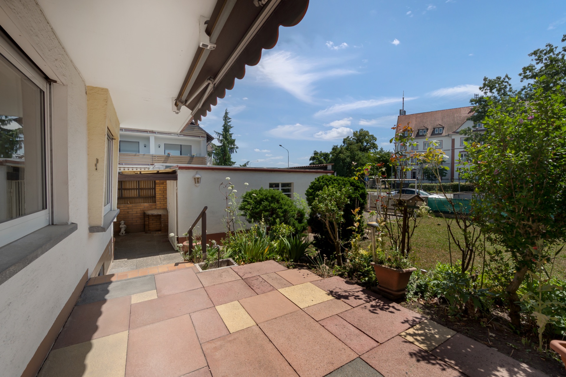 Gepflasterte Terrasse mit Blick auf Garten und angrenzende Gebäude an einem sonnigen Tag.