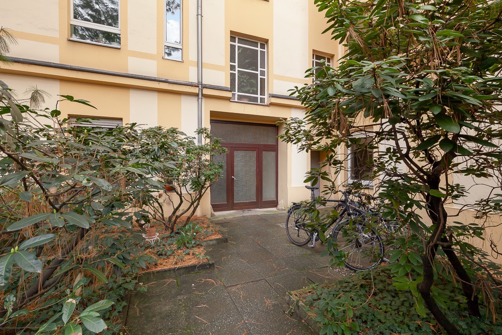 Hauseingang mit Glastür, Pflanzen und mehreren abgestellten Fahrrädern im Hof.