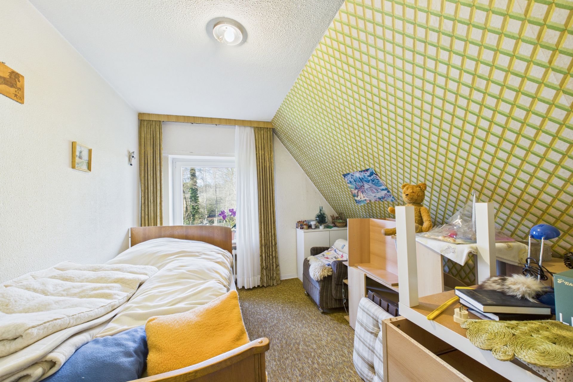 Kleines Schlafzimmer mit Bett, schräger Decke und Fenster, Regal mit Spielzeug und Büchern.