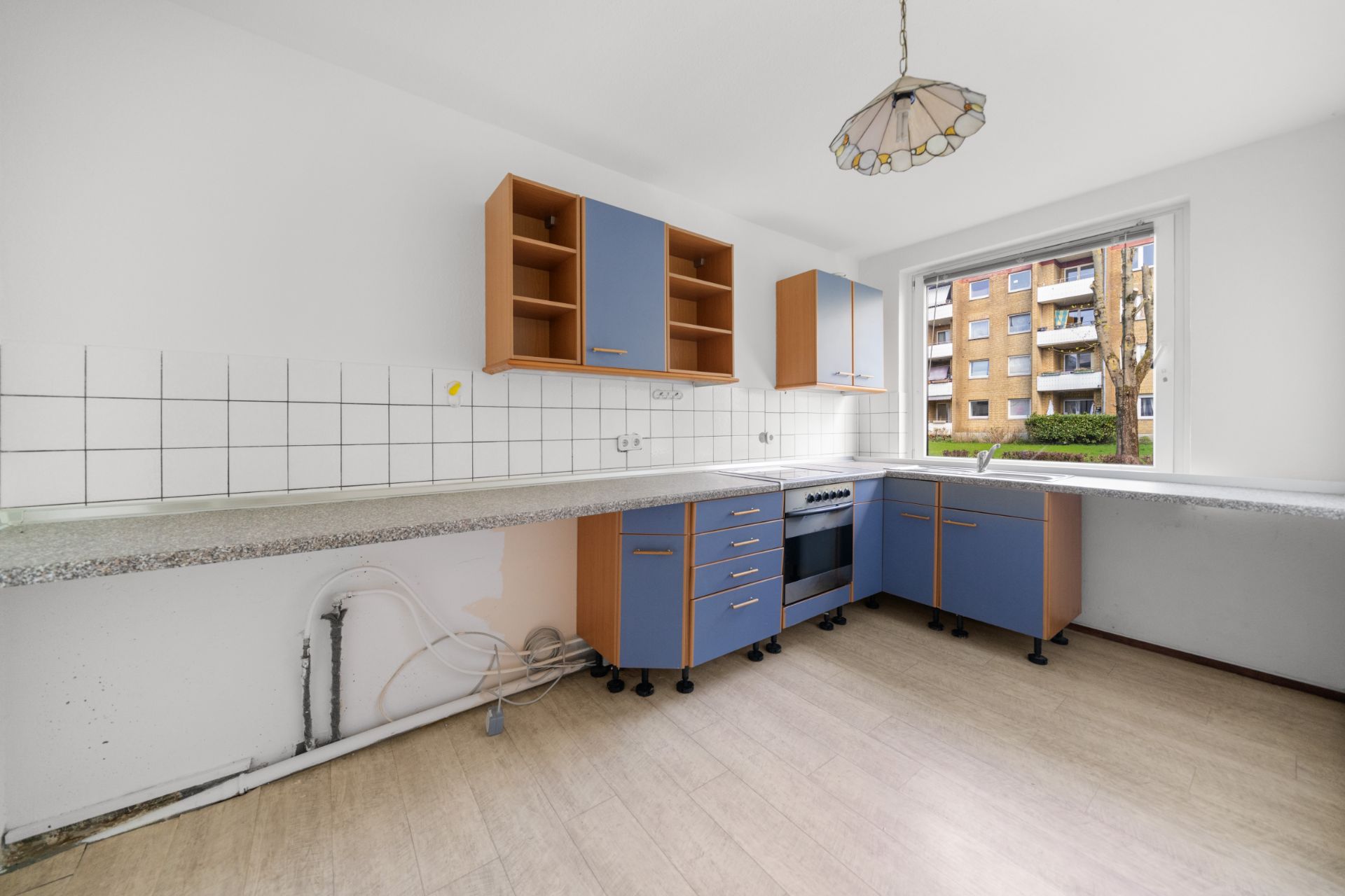 Leere Küche mit blauen Schränken, weißem Fliesenspiegel und großem Fenster.