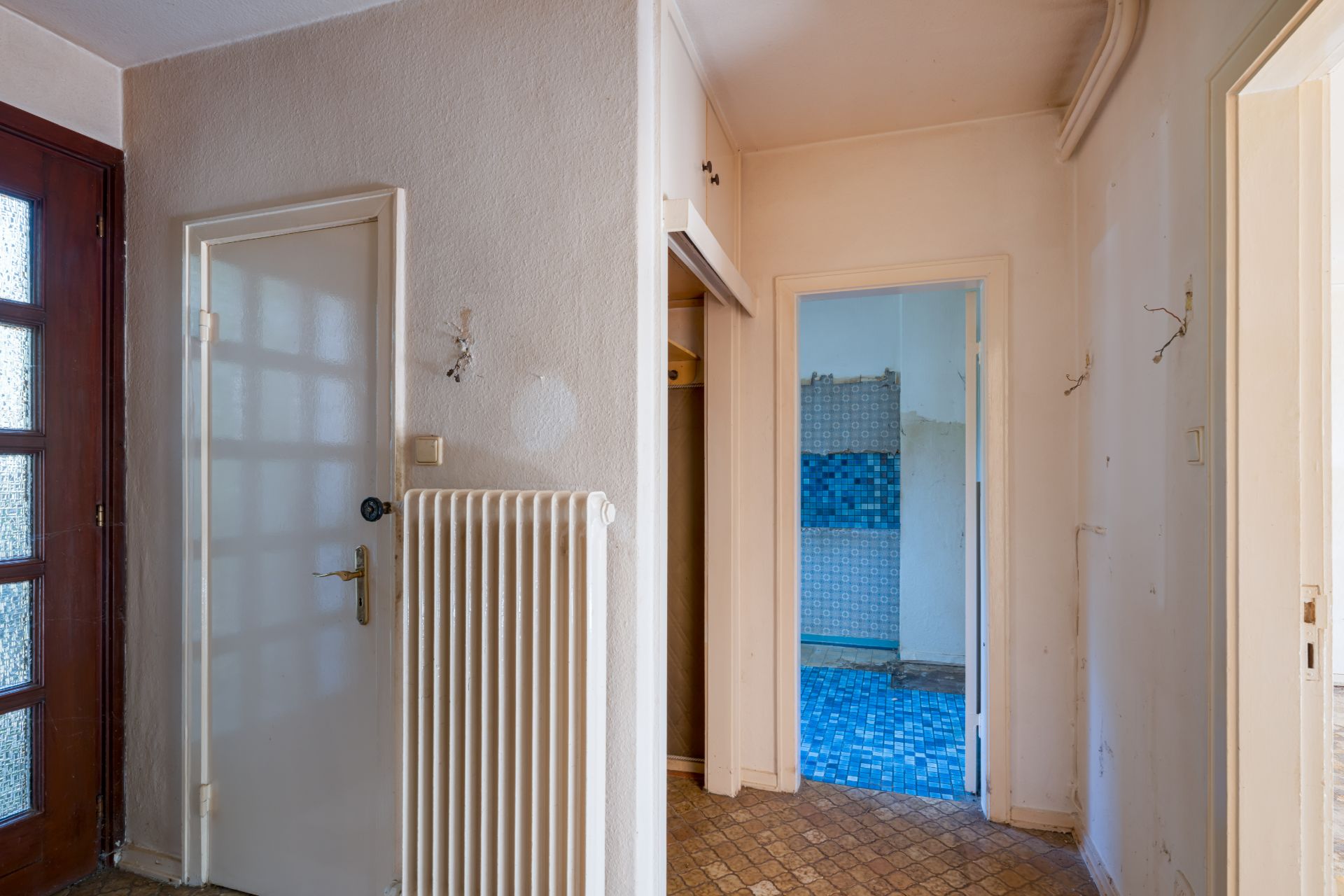 Flur mit Tür, Heizkörper und Blick ins Badezimmer mit blauen Fliesen.