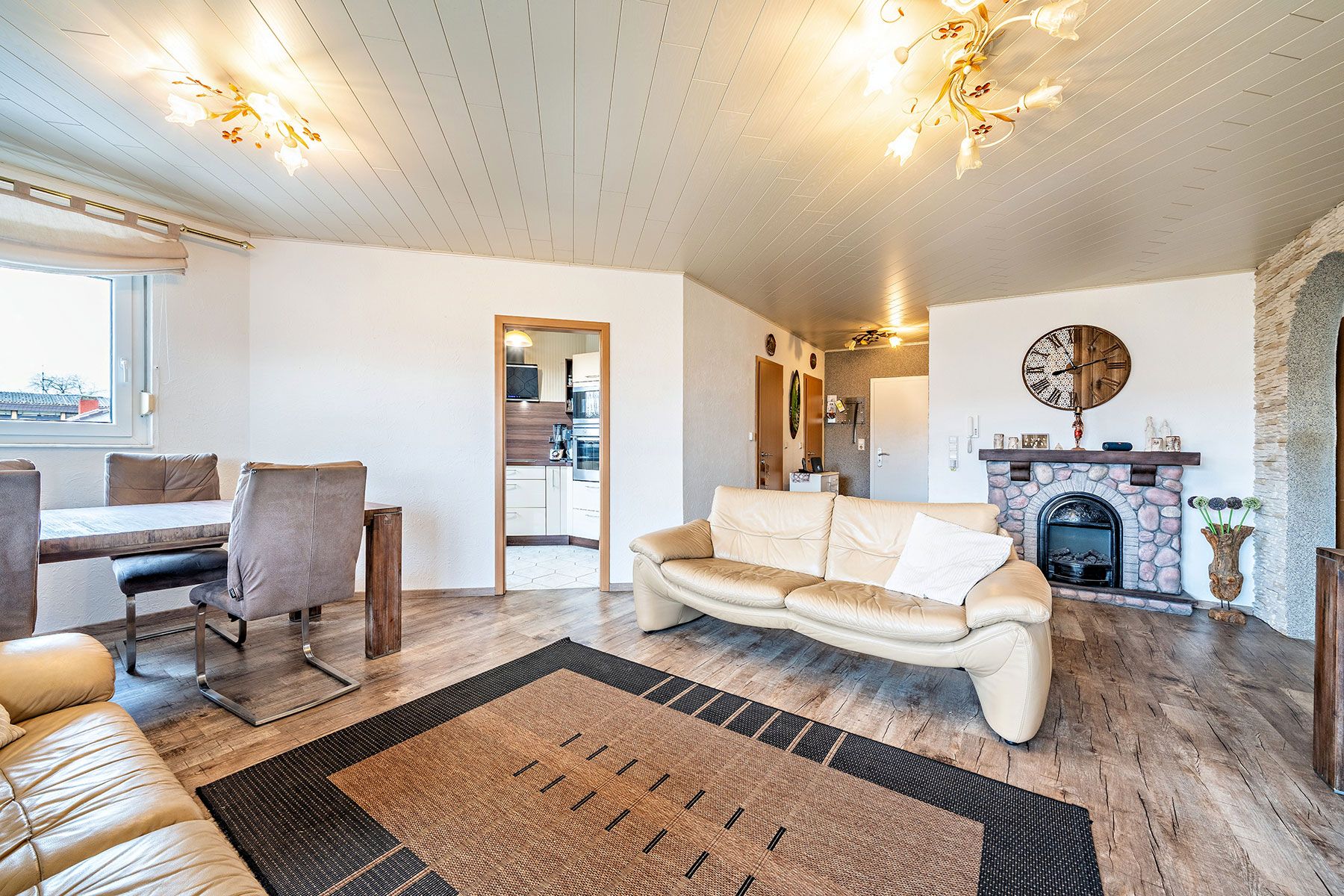 Helles Wohnzimmer mit Ledersofa, Esstisch, Kamin und Zugang zur Küche.