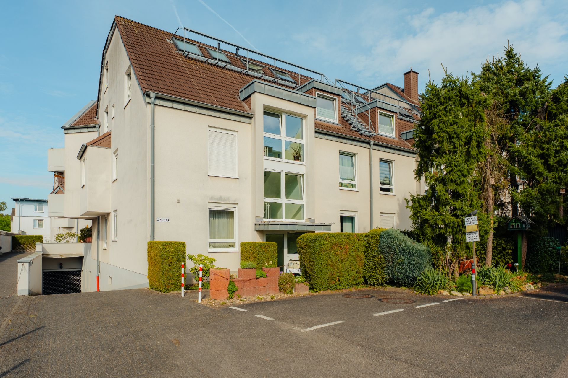 Modernes Mehrfamilienhaus mit weißer Fassade, braunem Dach und gepflegtem Vorgarten.