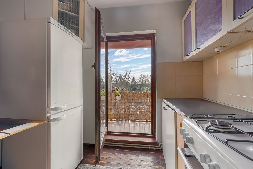 Kleine Küche mit Gasherd, Kühlschrank und offenem Zugang zu einem Balkon mit Ausblick ins Freie.