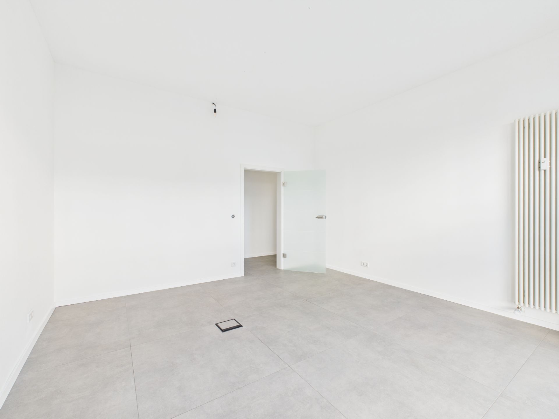 Leerer, heller Raum mit Fliesenboden, weißer Wand und Glastür.