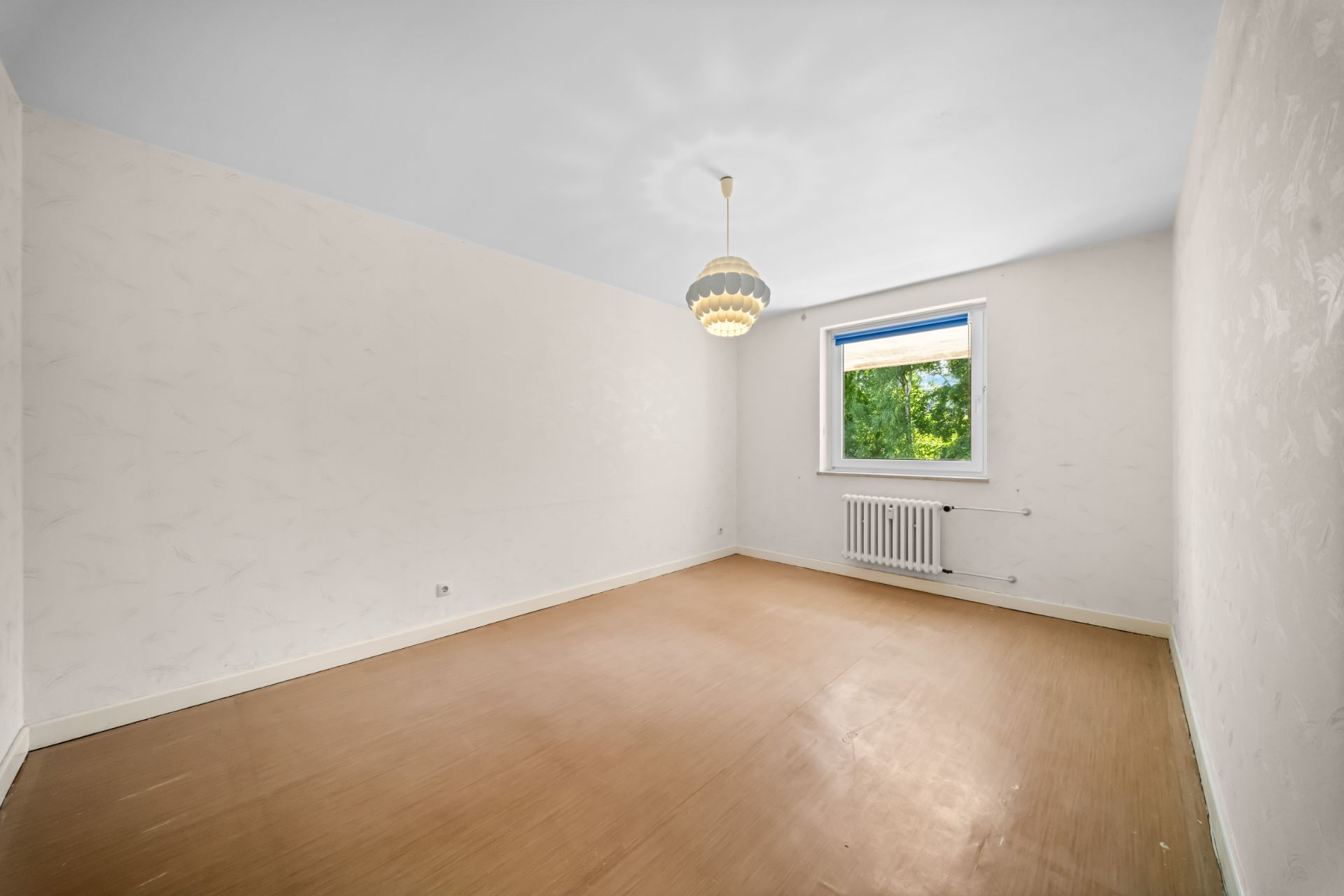 Leerer Raum mit hellem Boden, weißer Wand, Fenster und Heizkörper.