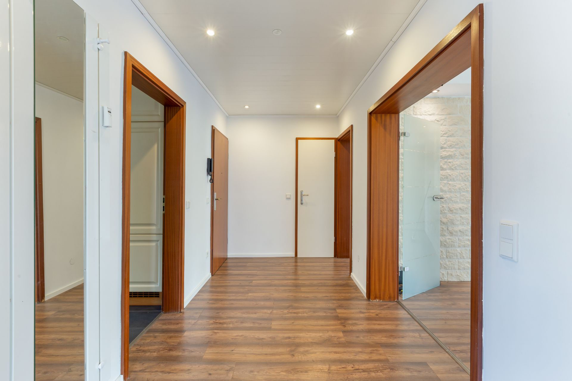 Heller Flur mit Holzfußboden und mehreren offenen Türen in einer Wohnung.