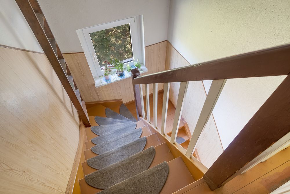 Holztreppe mit grauen Stufenmatten, Fenster mit Pflanzen auf der Fensterbank.
