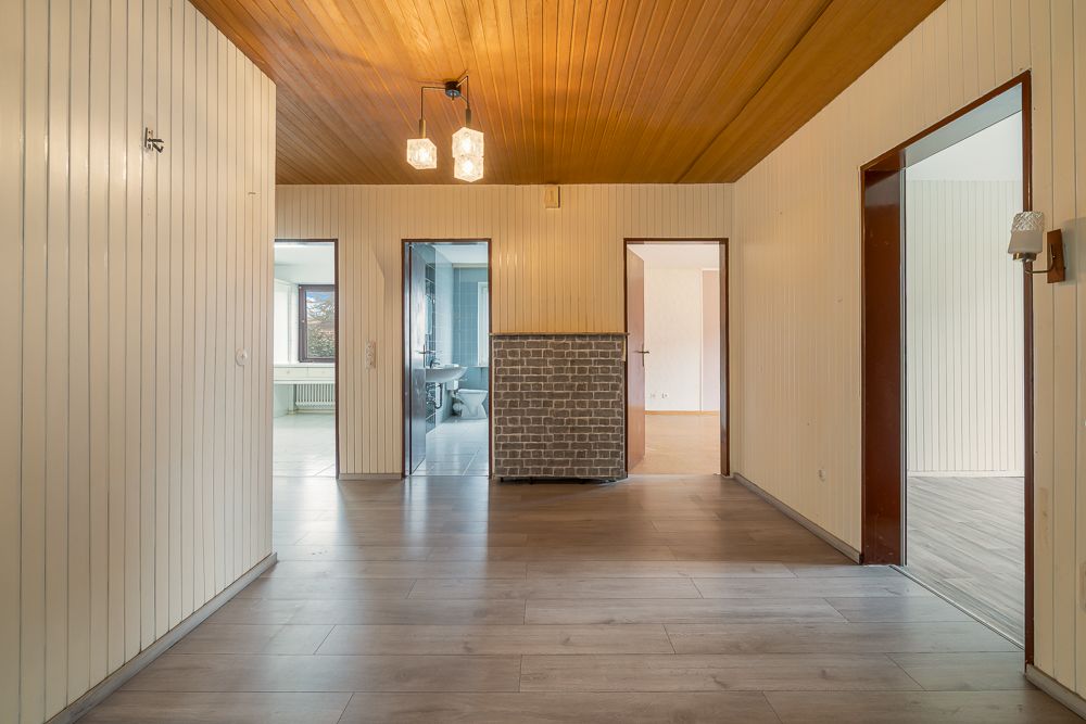 Wohnungsflur mit Holzdecke, drei offenen Türen und grauem Boden.