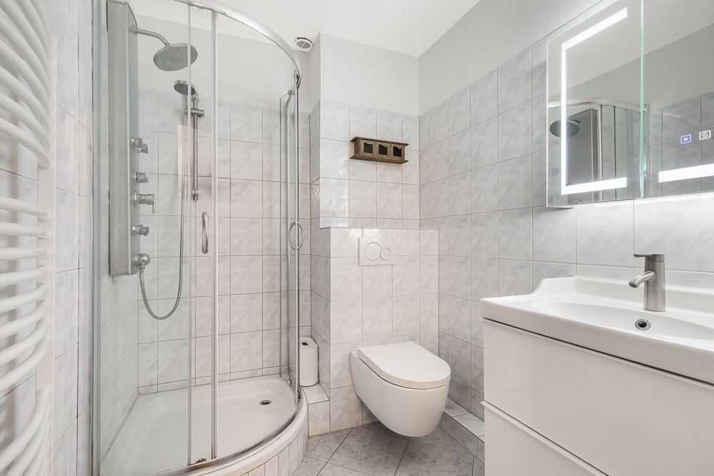 Modernes Bad mit Eckdusche, Wandtoilette, Waschbecken und beleuchtetem Spiegel.
