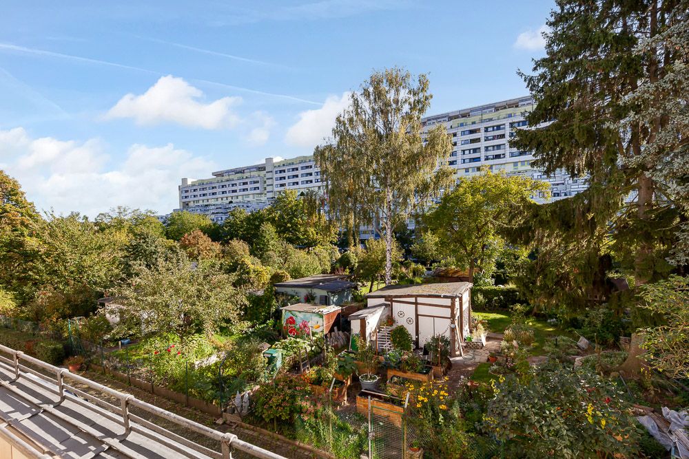 Blick auf einen Garten mit mehreren kleinen Häuschen und viel Grün, im Hintergrund ein Wohngebäude.
