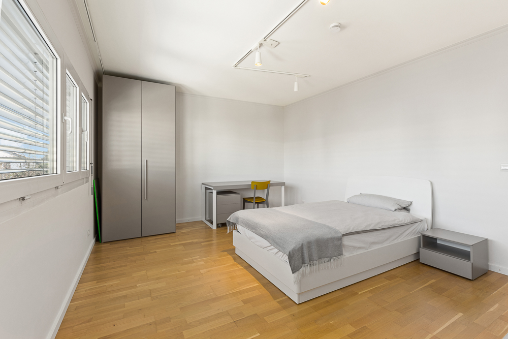Modernes Schlafzimmer mit Doppelbett, grauem Kleiderschrank, Schreibtisch und Nachttisch auf Parkettboden.
