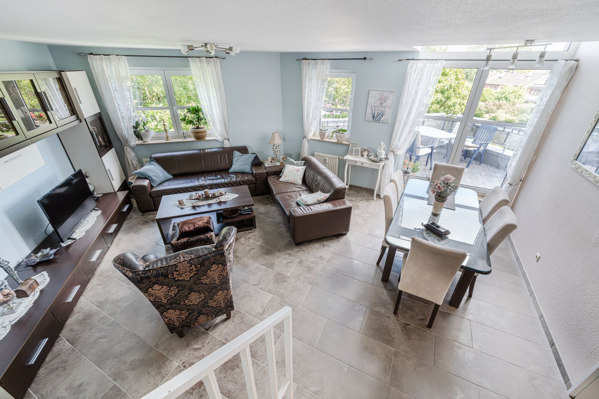 Helles Wohnzimmer mit Ledersofas, Esstisch, Fernseher und Zugang zum Balkon.