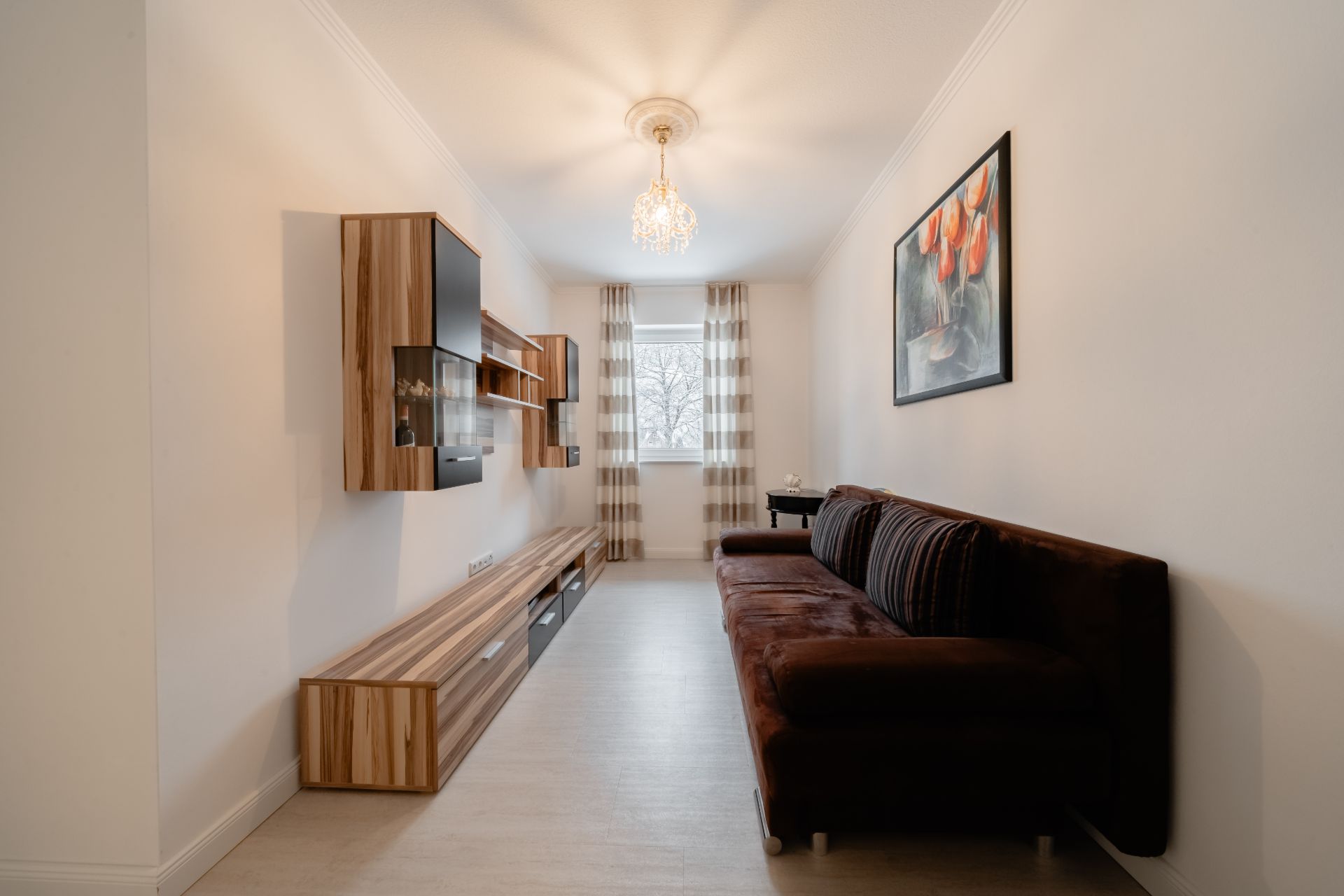 Helles Wohnzimmer mit braunem Sofa, Holzregalen, Fenster und Gemälde an der Wand.