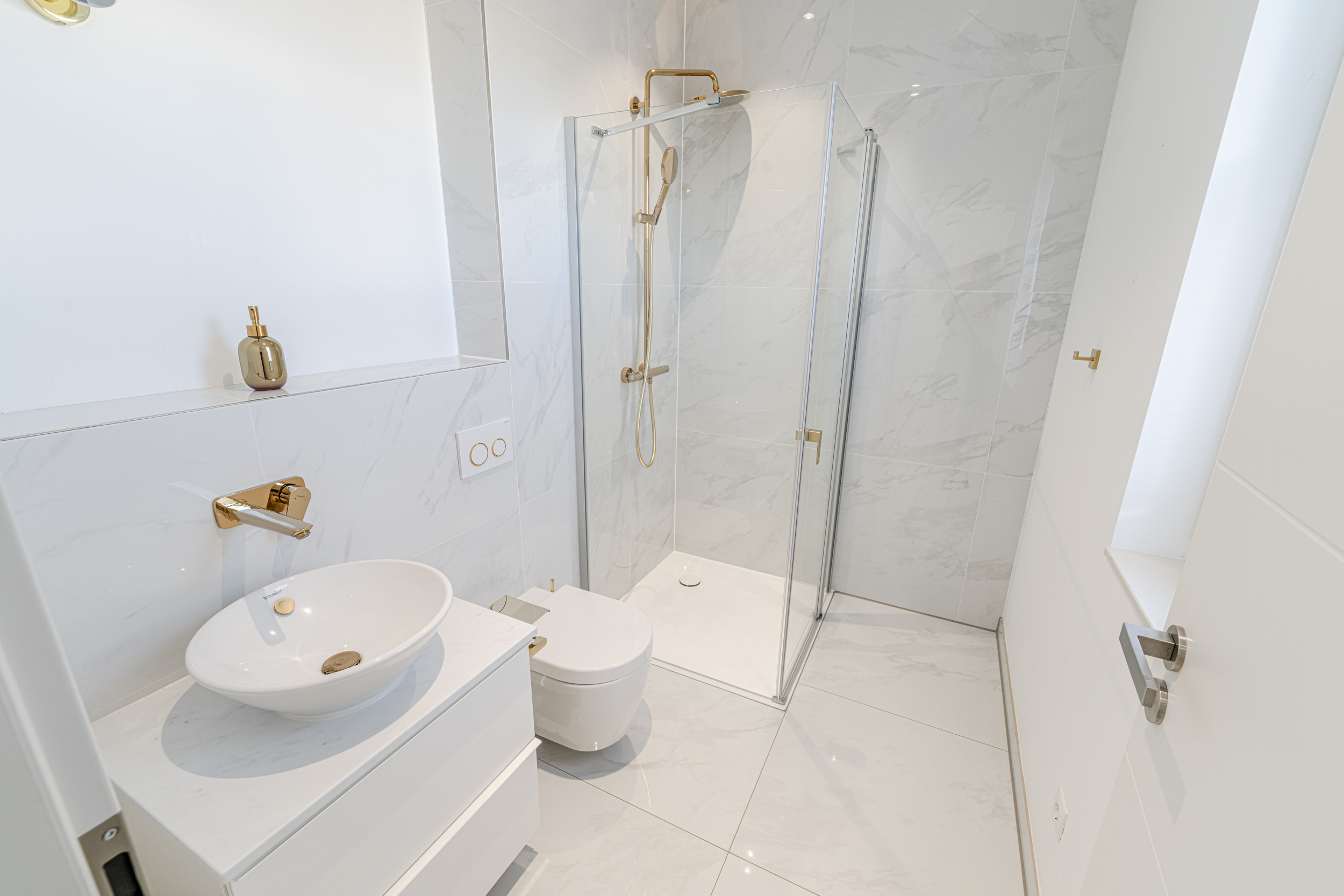 Modernes, weißes Badezimmer mit Dusche, Waschbecken, WC und goldenen Armaturen.