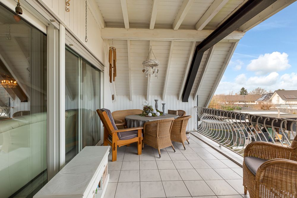 Überdachter Balkon mit Sitzgruppe aus Korbmöbeln und rundem Tisch, Blick nach draußen.