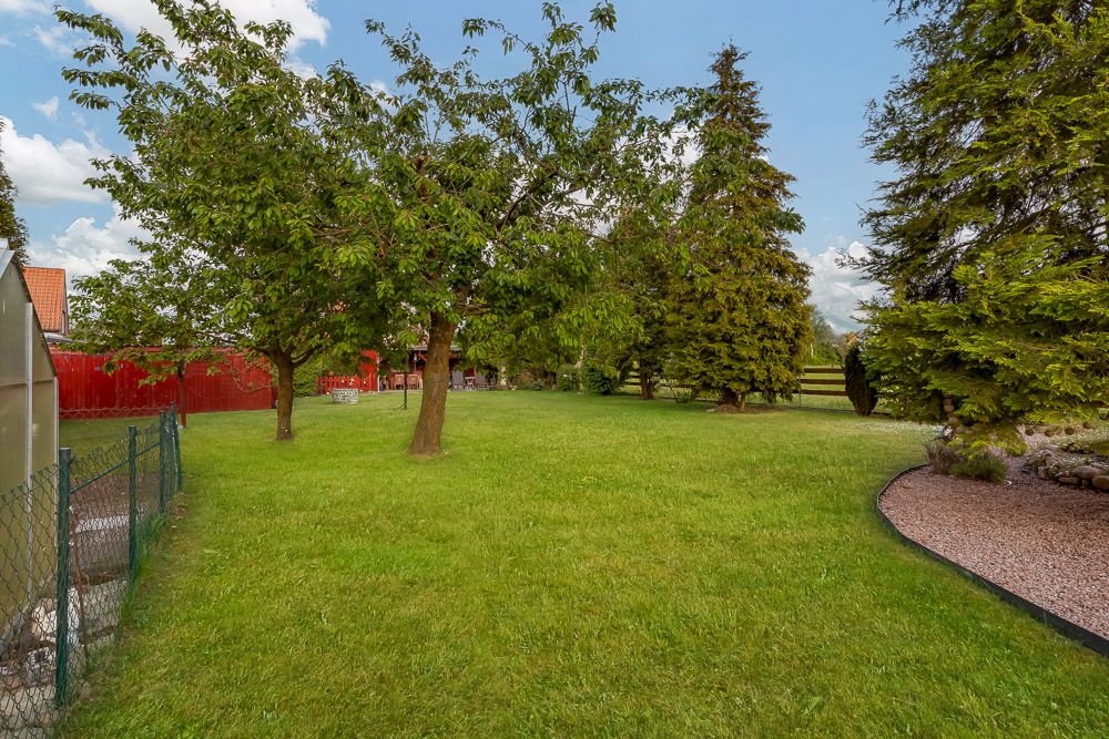 Großer Garten mit Rasenfläche, mehreren Bäumen und einem Zaun auf der linken Seite.