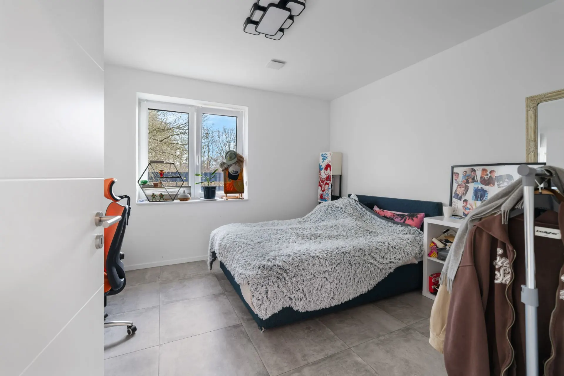 Helles Schlafzimmer mit großem Bett, Schreibtisch am Fenster und Kleiderständer.