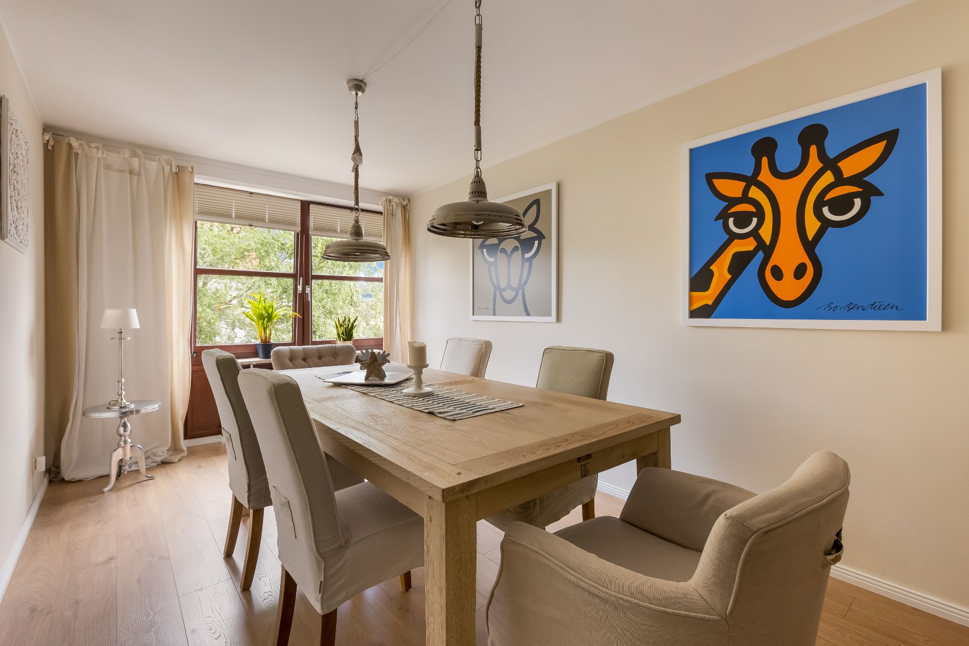 Esszimmer mit Holztisch, sechs Stühlen und buntem Giraffenbild an der Wand.
