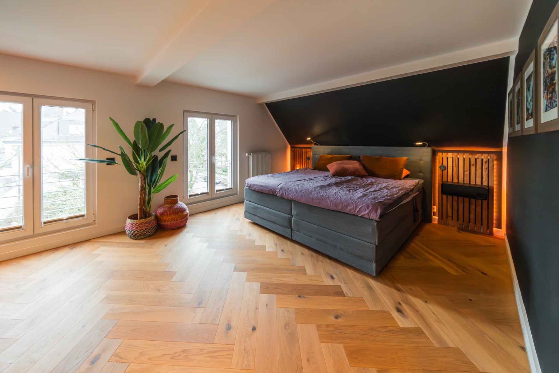 Modernes Schlafzimmer mit großem Bett, hellen Holzboden, Pflanze und Fenstern.