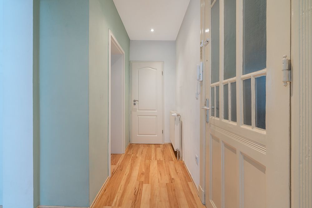 Heller Flur mit Holzboden, weißen Türen und grünlicher Wand in einem Wohnhaus.