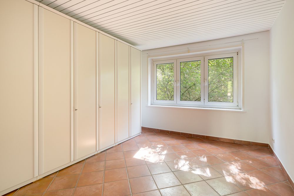 Helles Zimmer mit großen weißen Einbauschränken, Fenstern und terrakottafarbenen Fliesenboden.