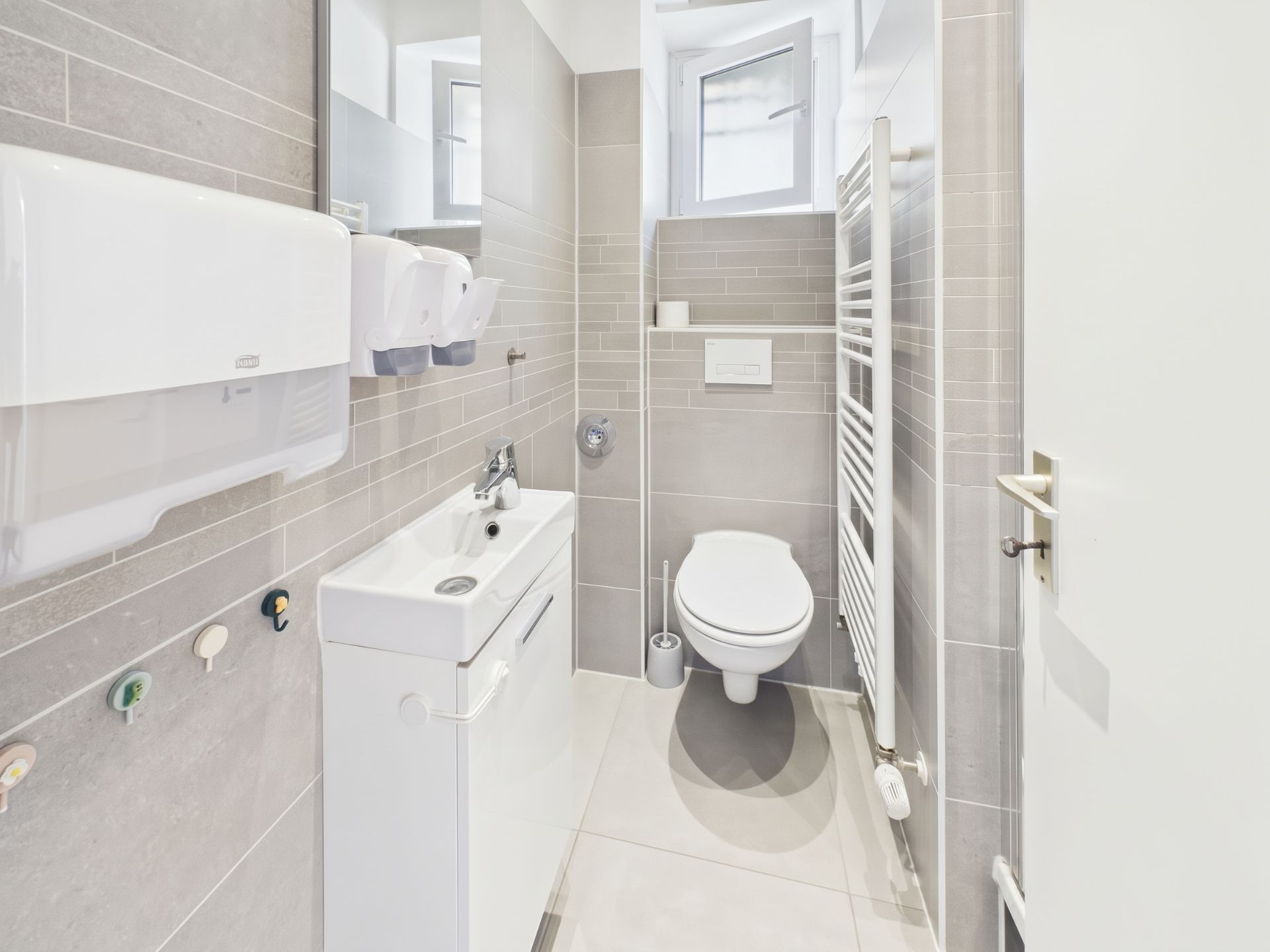 Modernes, kleines Bad mit Toilette, Waschbecken, Handtuchheizkörper und Fenster.