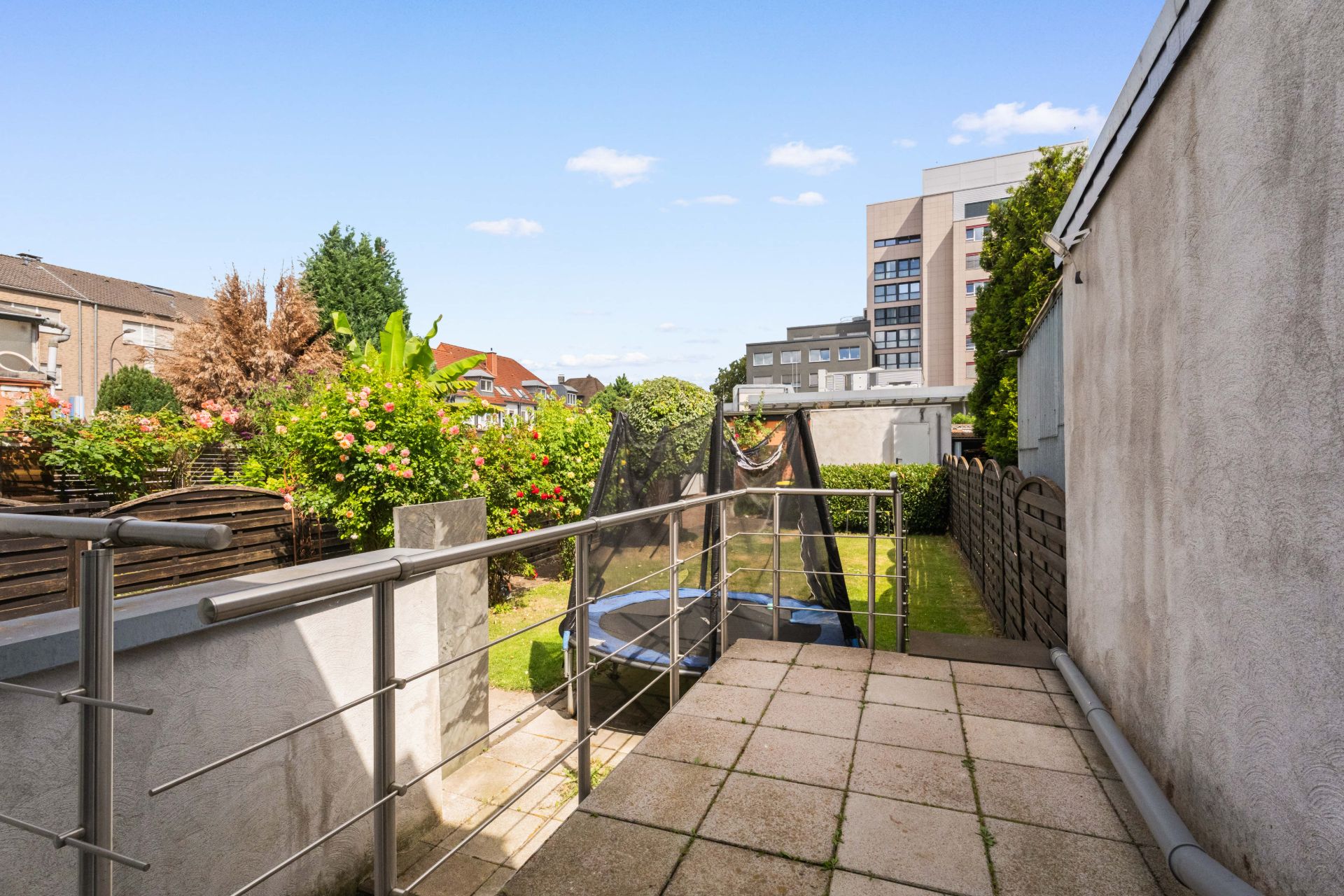 Terrasse mit Metallgeländer, Blick auf Garten mit Trampolin und Büschen.