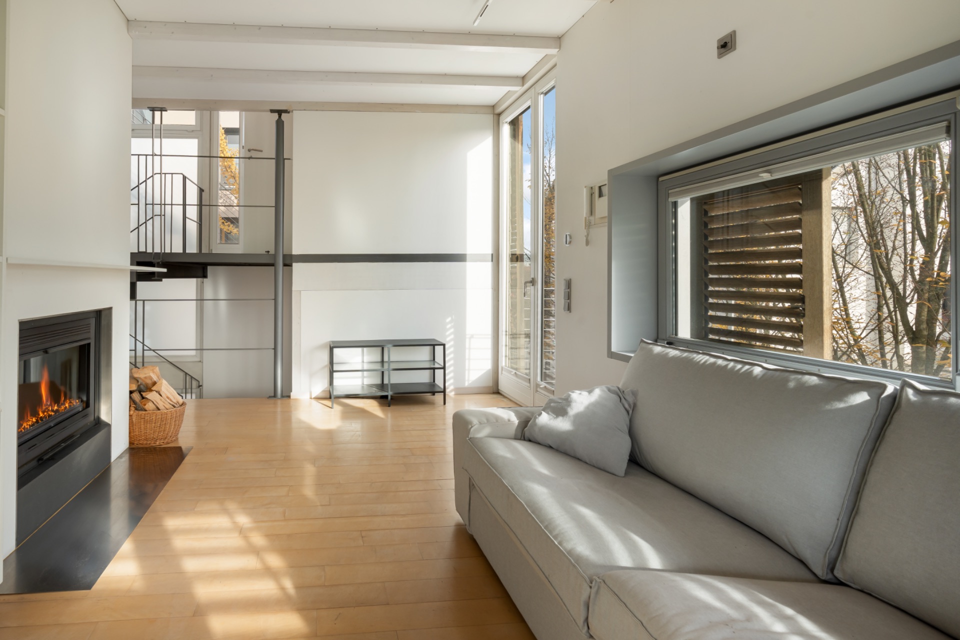 Helles Wohnzimmer mit Kamin, grauem Sofa, Holzboden und Zugang zum Balkon.