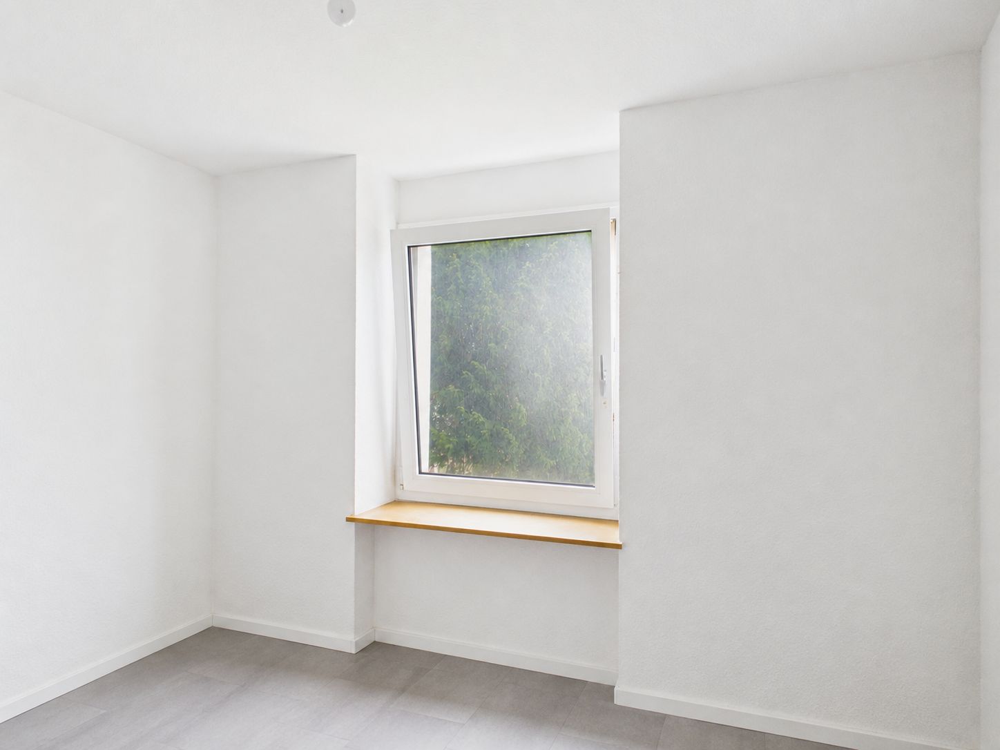 Helles, leeres Zimmer mit weiß gestrichenen Wänden und einem Fenster mit Holzfensterbank.