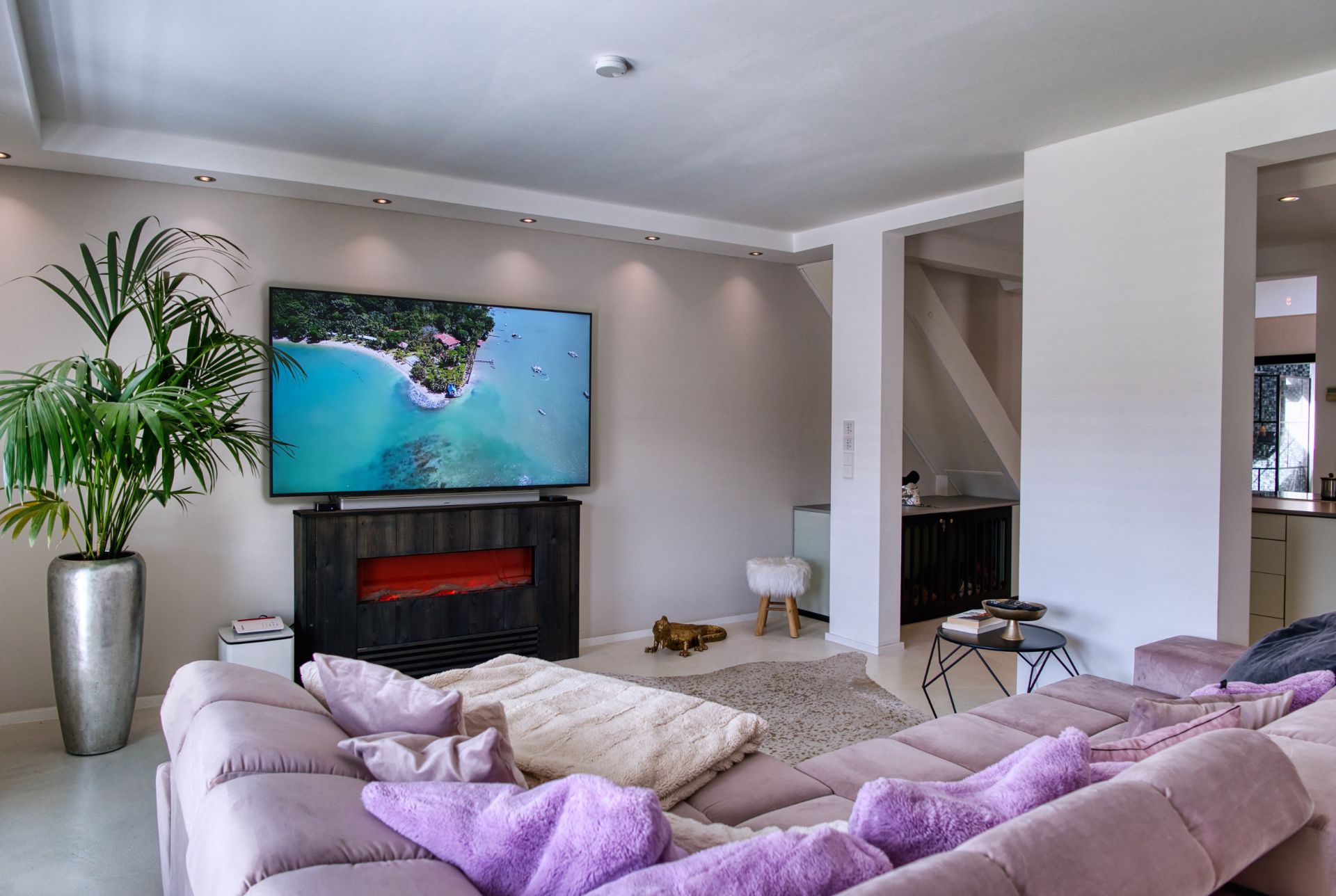 Modernes Wohnzimmer mit hellviolettem Sofa, großem Fernseher und einer grünen Zimmerpflanze.