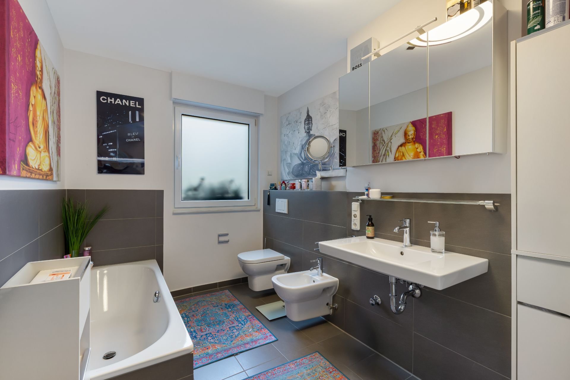 Modernes Badezimmer mit Badewanne, Waschbecken, WC, Bidet und farbigen Teppichen.